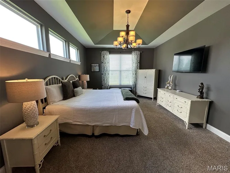 Spacious room featuring a tray ceiling with a central chandelier, high transom windows, and wall-to-wall carpeting — 110 Alta Mira Court, Dardenne Prairie, MO 63368