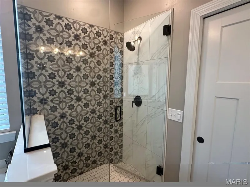 Spacious walk-in shower featuring patterned wall tiling, a glass enclosure, and matte black fixtures — 110 Alta Mira Court, Dardenne Prairie, MO 63368