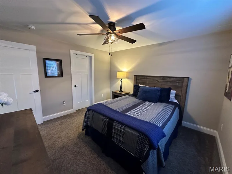 Bedroom featuring textured carpeting, a rustic wood-finish headboard, a ceiling fan with integrated lighting, and two interior doors with black hardware — 110 Alta Mira Court, Dardenne Prairie, MO 63368