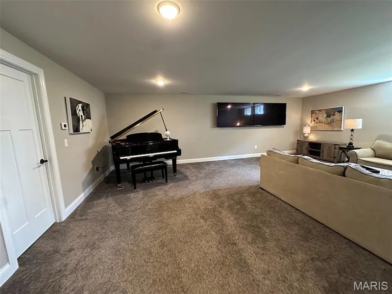 Spacious basement recreation room featuring a grand piano, built-in cabinetry with display shelving, recessed ceiling lighting, wall-mounted flat-screen television, neutral carpet flooring, and finished walls with multiple entry points — 110 Alta Mira Court, Dardenne Prairie, MO 63368