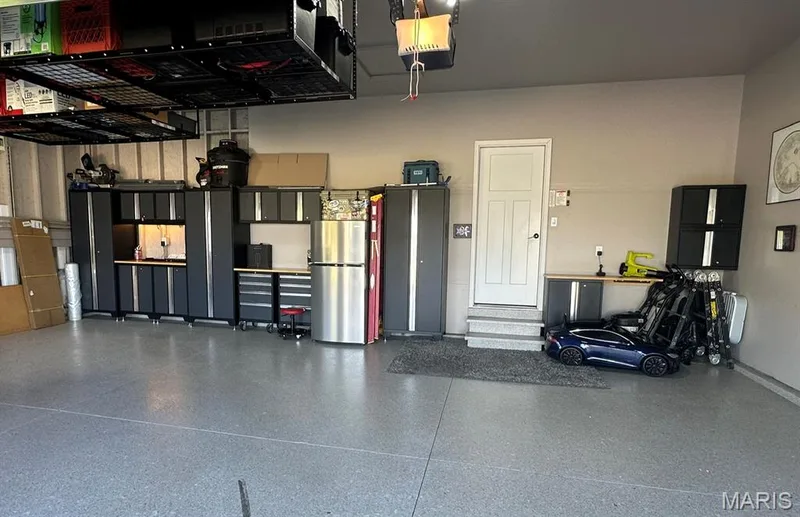 Garage featuring an epoxy coated floor, extensive built-in cabinetry, overhead storage racks, a utility sink, and a stainless steel refrigerator — 110 Alta Mira Court, Dardenne Prairie, MO 63368