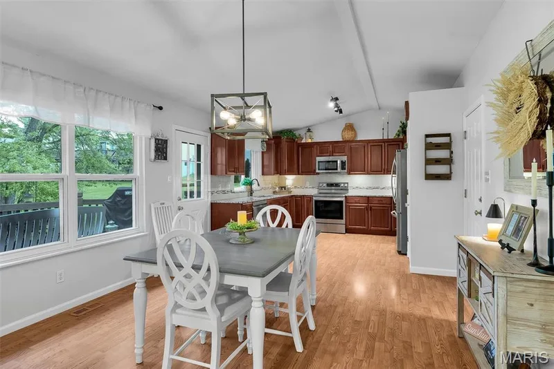 Open-concept dining area with wood-finish flooring, a contemporary chandelier, and a large window — 104 Cedar Crest Court, St Charles, MO 63304