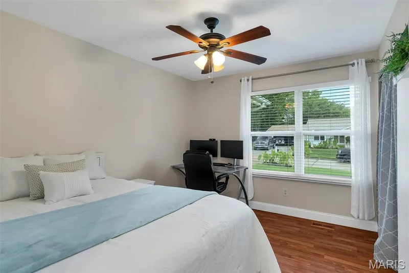 Bright secondary bedroom featuring warm wood-finish flooring, ceiling fan with integrated lighting, and white painted door frames — 104 Cedar Crest Court, St Charles, MO 63304