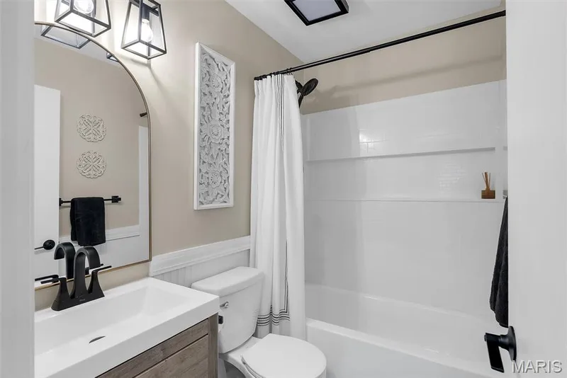 Modern bathroom featuring a updated vanity with rectangular vessel sink and matte black fixtures, white subway tile surround with horizontal stripe detail, frameless mirror with integrated lighting, and a combined shower-tub with glass enclosure and chrome fixtures — 104 Cedar Crest Court, St Charles, MO 63304
