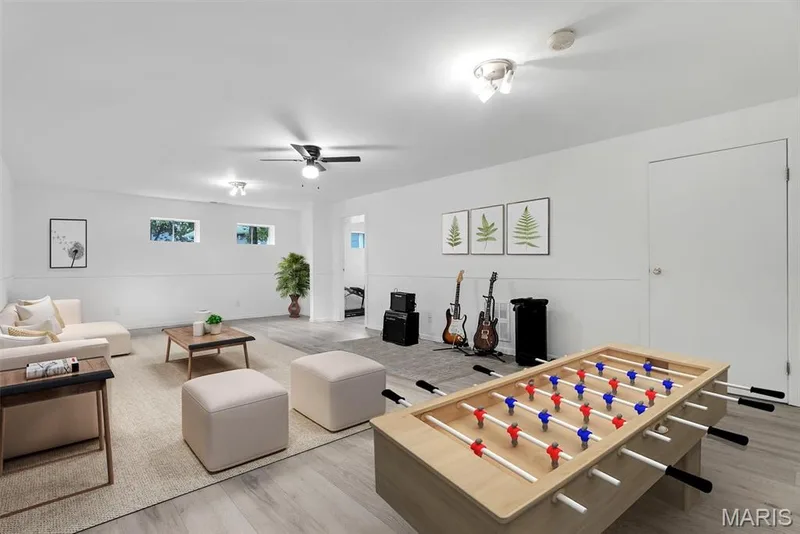 Virtually Staged Basement showing versatile recreation room featuring engineered wood-finish flooring, recessed and ceiling fan lighting, white shaker-style cabinetry, and ample space for multiple activity stations — 104 Cedar Crest Court, St Charles, MO 63304