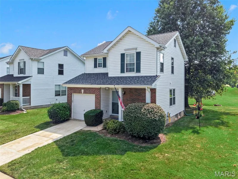 Classic two-story Colonial featuring white vinyl siding, brick front entry with covered porch, and a two-car attached garage — 669 Homerun Drive, O'Fallon, MO 63366