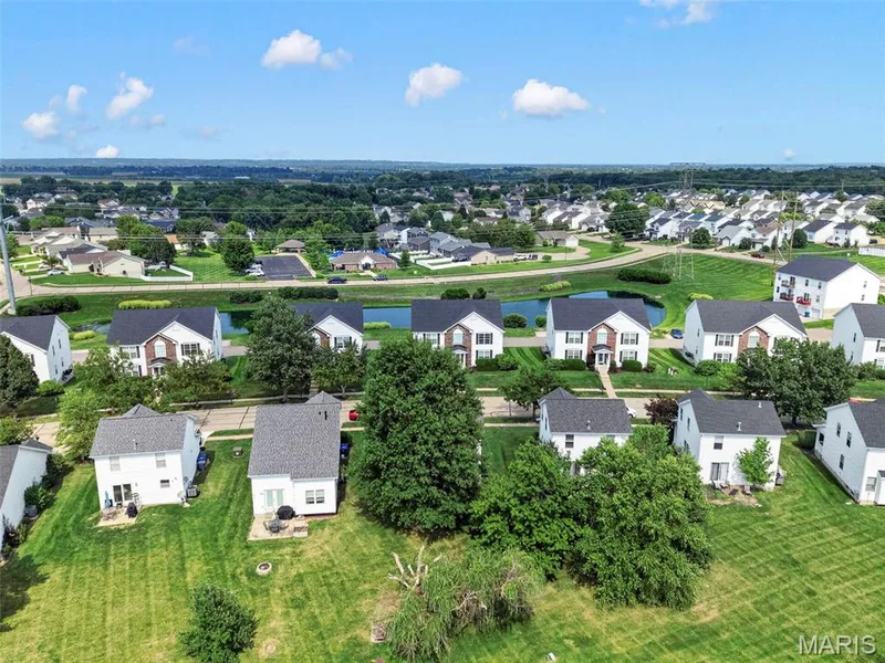 Aerial view of a residential community featuring multiple homes with dark roofs and light-colored siding, manicured green lawns, and mature trees — 669 Homerun Drive, O'Fallon, MO 63366
