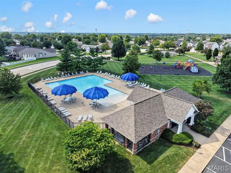 Outdoor swimming pool with surrounding lounge seating, adjacent clubhouse building, and a nearby playground area — 669 Homerun Drive, O'Fallon, MO 63366
