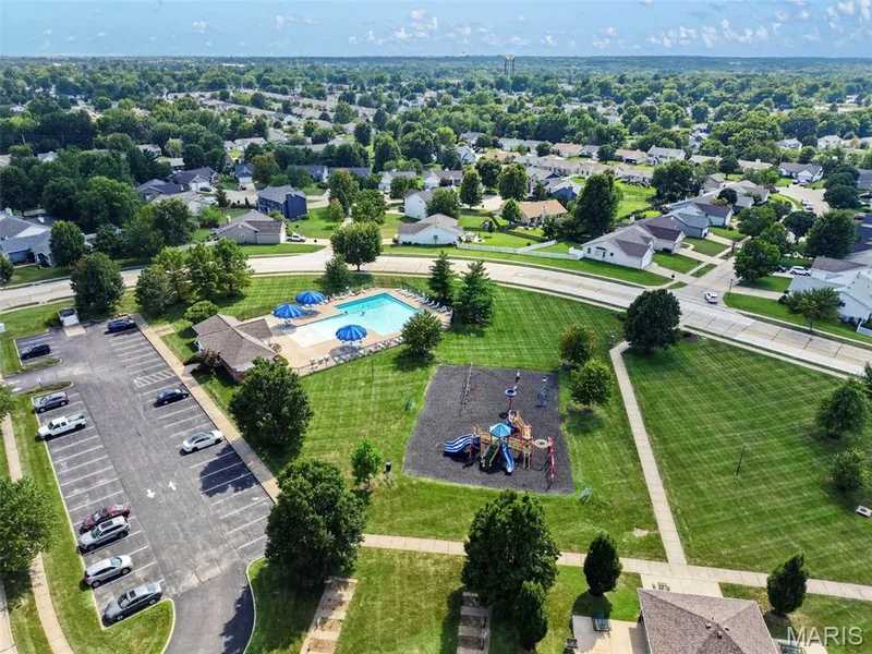 Community pool with a surrounding patio, adjacent clubhouse, and nearby playground — 669 Homerun Drive, O'Fallon, MO 63366