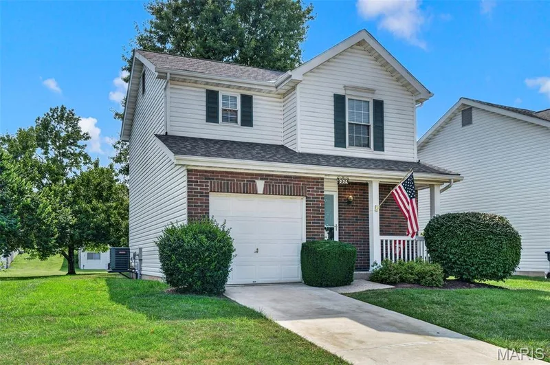 Two-story residence featuring white siding and brick accents, an attached garage, a covered front porch, and a paved driveway — 669 Homerun Drive, O'Fallon, MO 63366
