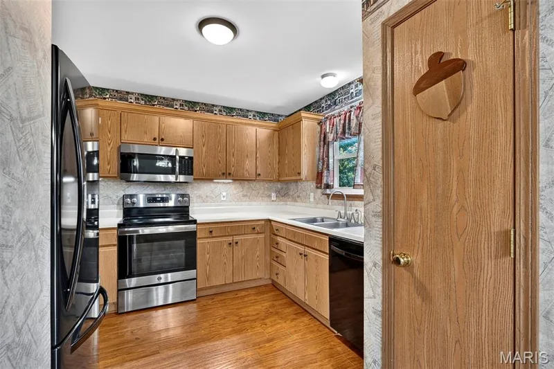 Wood-finish cabinetry, stainless steel appliances, white countertops, wood-finish flooring, and a double basin sink — 669 Homerun Drive, O'Fallon, MO 63366