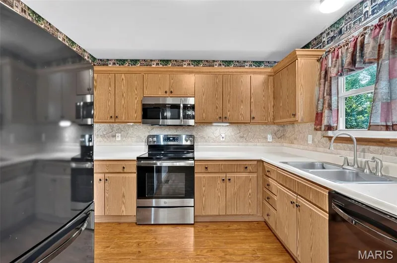 Kitchen featuring wood-finish cabinetry, stainless steel appliances, a double basin sink, and wood-finish flooring — 669 Homerun Drive, O'Fallon, MO 63366
