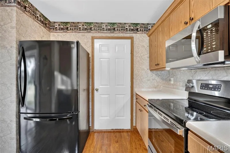 Wood-finish flooring, light wood cabinetry, stainless steel microwave, black electric range, and solid surface countertops — 669 Homerun Drive, O'Fallon, MO 63366