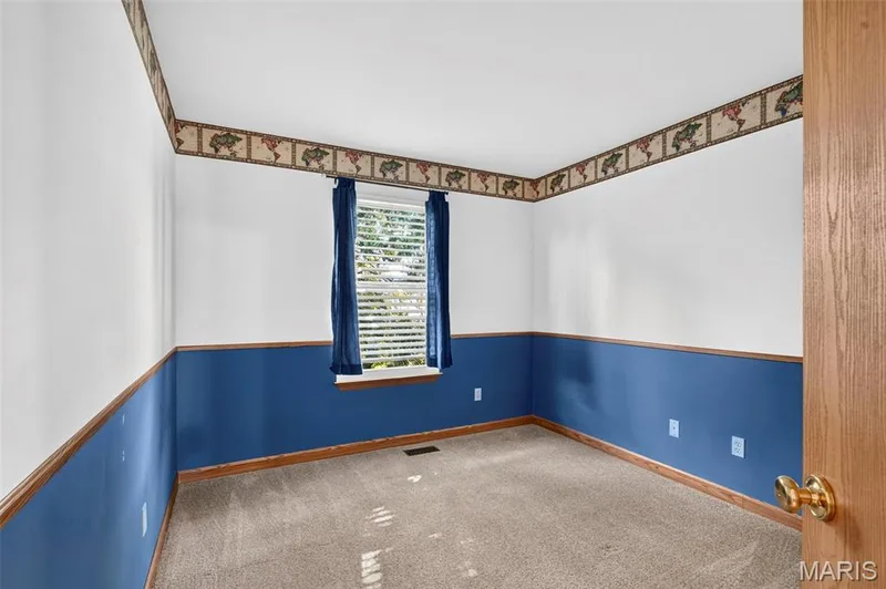 Room with neutral carpet, white walls, and a blue lower wall section, featuring a single window with blinds and blue drapes — 669 Homerun Drive, O'Fallon, MO 63366