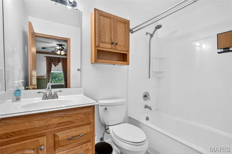 Bright bathroom featuring a wood-finish vanity with an undermount sink and chrome faucet, white subway tile surround, ceramic toilet, and an integrated bathtub-shower combination with chrome fixtures and grab bar — 669 Homerun Drive, O'Fallon, MO 63366