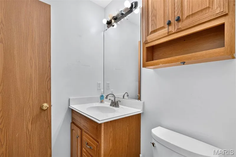 Bathroom featuring a wood-finish vanity with a white countertop and integrated sink, wall-mounted mirror, and overhead lighting — 669 Homerun Drive, O'Fallon, MO 63366