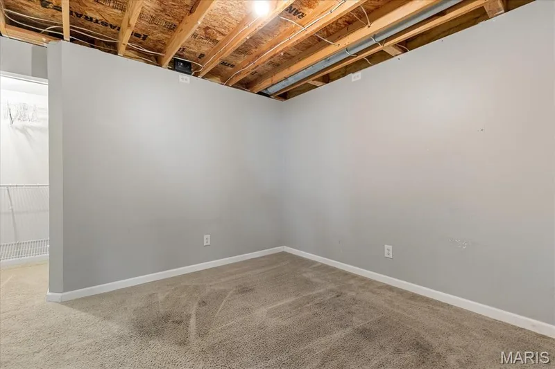 Partially finished lower level bonus room featuring carpeted flooring, drywall, and direct access to the storage area, ideal for a den or sleeping area. — 146 Tuscany Lane, Wentzville, MO 63385