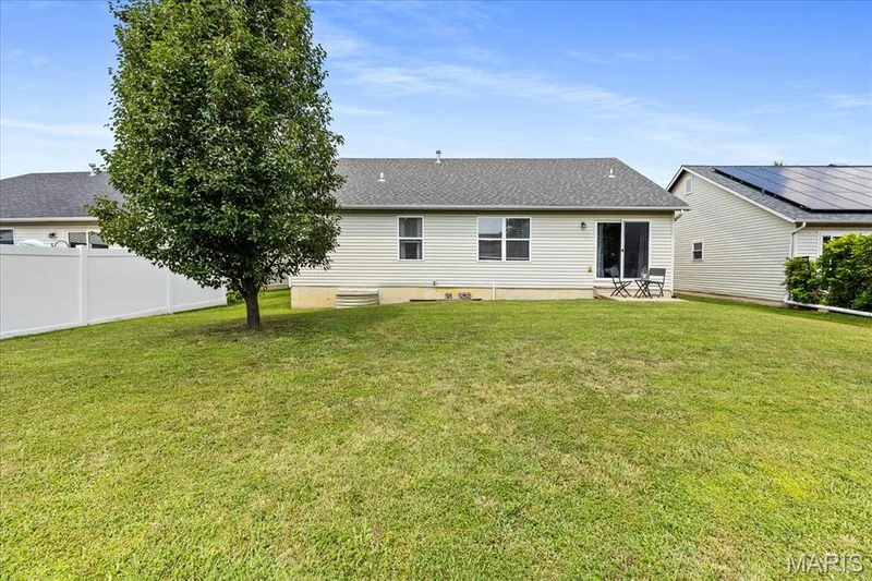 Expansive, level backyard featuring a concrete patio, mature shade tree, and white vinyl privacy fencing along the side. — 146 Tuscany Lane, Wentzville, MO 63385