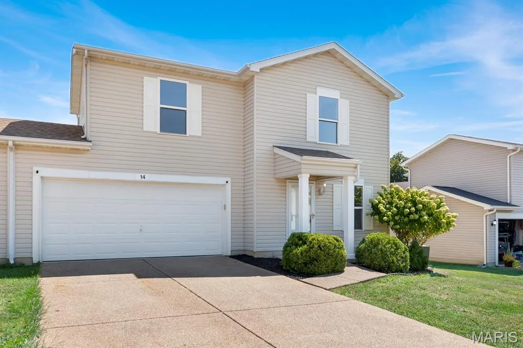 Two-story residence featuring siding exterior, an attached two-car garage, covered entry with columns, and mature shrubbery — 14 Bridgeton Court, Wentzville, MO 63385