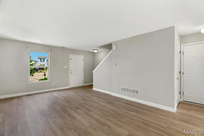 Wood-finish flooring throughout the main living area, staircase with carpeted treads, and a wall-mounted light fixture — 14 Bridgeton Court, Wentzville, MO 63385