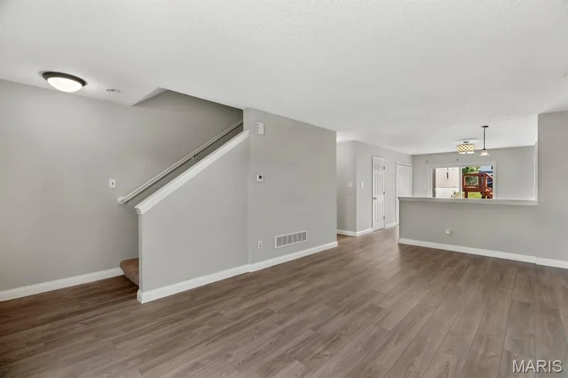 Wood-finish flooring throughout the main living area, staircase with carpeted treads, and a wall-mounted light fixture — 14 Bridgeton Court, Wentzville, MO 63385