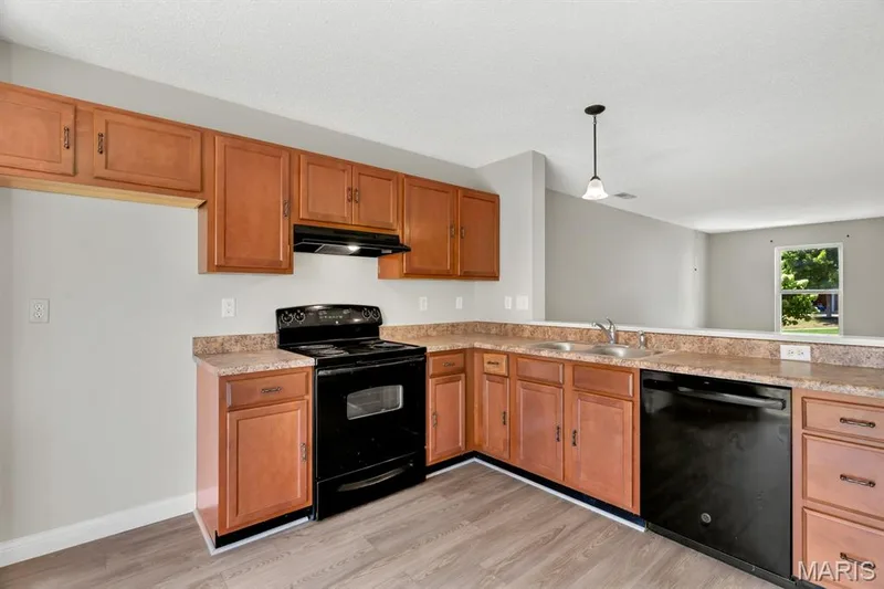 Kitchen featuring wood-finish cabinetry, built-in range, dual basin sink, and a dishwasher — 14 Bridgeton Court, Wentzville, MO 63385