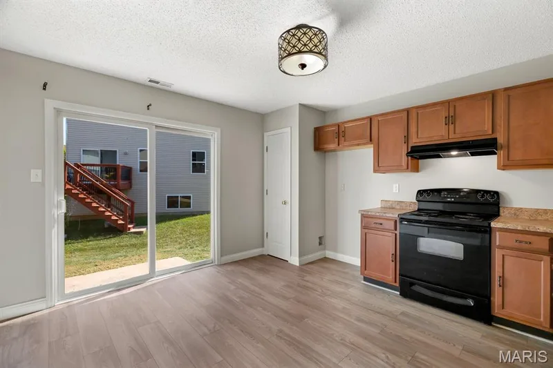 Wood-finish flooring, sliding glass patio door, backyard with deck, wood cabinetry, and black electric range — 14 Bridgeton Court, Wentzville, MO 63385