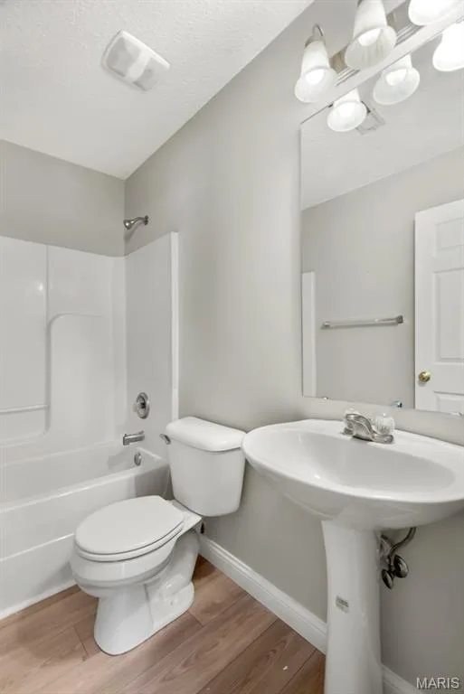 Full bathroom featuring a white pedestal sink, toilet, tub with shower, and wood-finish flooring — 14 Bridgeton Court, Wentzville, MO 63385