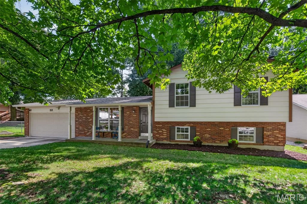 Split-level home featuring a brick and siding exterior with a attached garage, front entry with brick detailing, and multiple window placements — 23 Crescent Woods Drive, St Peters, MO 63376