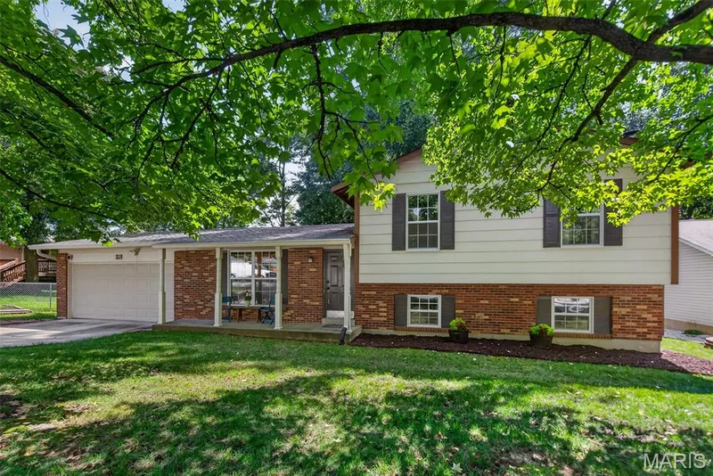 Split-level home featuring a brick and siding exterior with a attached garage, front entry with brick detailing, and multiple window placements — 23 Crescent Woods Drive, St Peters, MO 63376