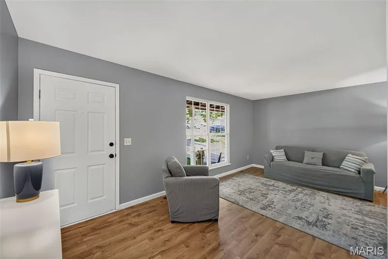Bright and spacious living area showcasing laminate hardwood flooring, gray walls, and abundant natural light from large windows — 23 Crescent Woods Drive, St Peters, MO 63376