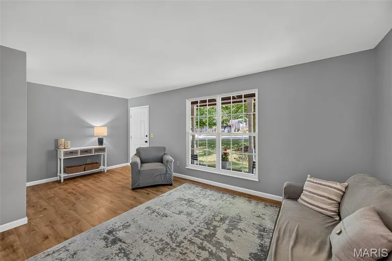 Bright and spacious living room featuring laminate wood-finish flooring, soft gray walls, and abundant natural light from large multi-pane windows — 23 Crescent Woods Drive, St Peters, MO 63376