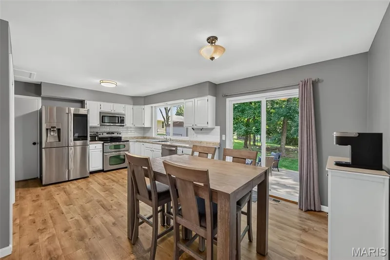 Open-concept kitchen and dining area featuring stainless steel appliances, white cabinetry with laminate hardware accents, wood-finish flooring throughout — 23 Crescent Woods Drive, St Peters, MO 63376