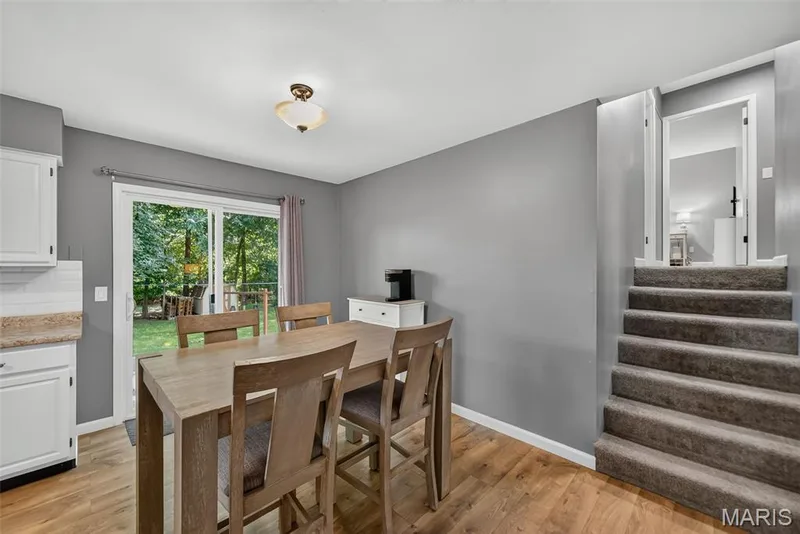 Dining area featuring laminate wood-finish flooring, a sliding glass door to the exterior, white shaker-style cabinetry, and light grey walls — 23 Crescent Woods Drive, St Peters, MO 63376