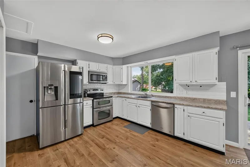 Modern kitchen featuring stainless steel appliances, white cabinetry, wood-finish flooring, a neutral countertop, and a white subway tile backsplash — 23 Crescent Woods Drive, St Peters, MO 63376