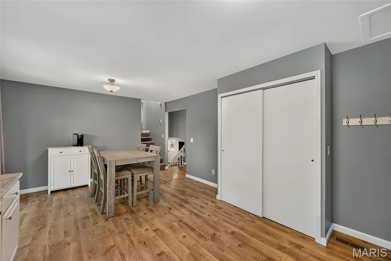 Open-concept room featuring laminate wood-finish flooring, neutral gray walls, a built-in pantry closet with sliding white doors, and a staircase — 23 Crescent Woods Drive, St Peters, MO 63376