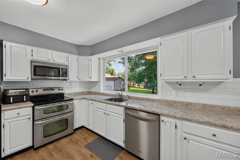 Kitchen featuring white cabinetry, stainless steel appliances, a white subway tile backsplash, and laminate wood-finish flooring — 23 Crescent Woods Drive, St Peters, MO 63376