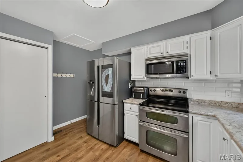 Kitchen featuring stainless steel appliances, white cabinetry, light-toned countertops, white subway tile backsplash, and laminate wood-finish flooring — 23 Crescent Woods Drive, St Peters, MO 63376
