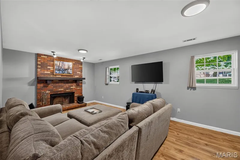 Spacious recreation room featuring a brick fireplace with mantel, recessed ceiling lighting, and hardwood flooring — 23 Crescent Woods Drive, St Peters, MO 63376