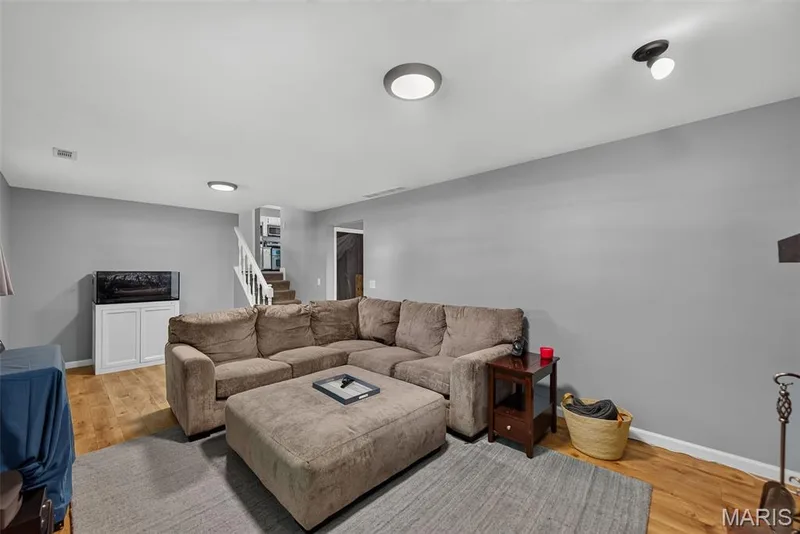 Finished basement recreation room featuring laminate wood-finish flooring, neutral gray walls, recessed ceiling lighting, and a large ottoman — 23 Crescent Woods Drive, St Peters, MO 63376