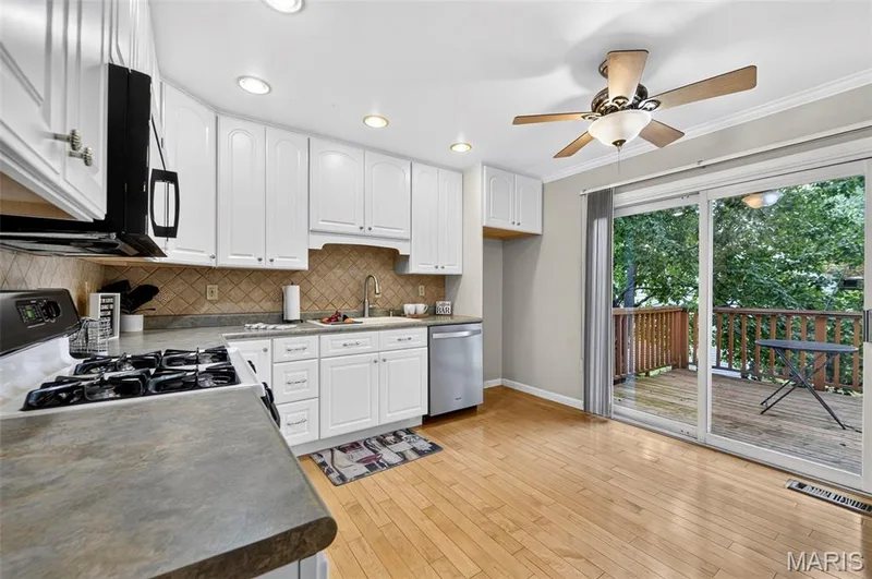 Kitchen featuring white cabinetry, a neutral-toned tile backsplash, and light wood-finish flooring — 1319 Brandywine Lane, St Peters, MO 63376