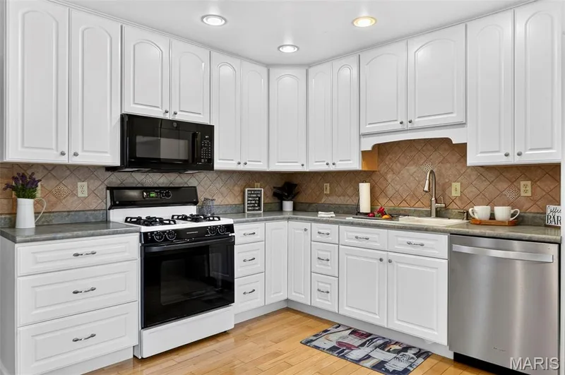 Bright kitchen featuring white cabinetry, a tile backsplash, recessed lighting, wood-finish flooring, and stainless steel appliances — 1319 Brandywine Lane, St Peters, MO 63376