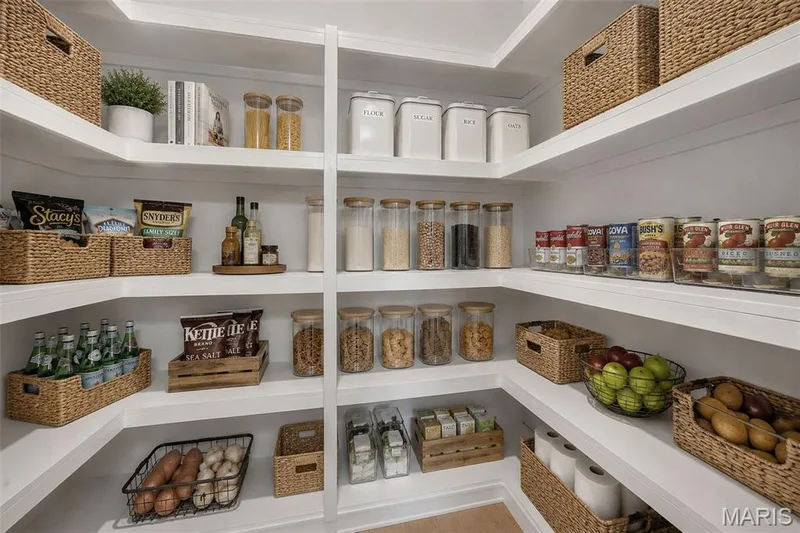 Fully Organized Walk-In Pantry featuring custom white shelving with woven storage baskets, glass and ceramic food storage containers, and dedicated zones for dry goods, fresh produce, and pantry staples — 1319 Brandywine Lane, St Peters, MO 63376