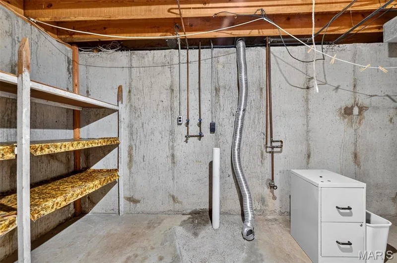 Unfinished basement featuring exposed wood joists and concrete walls, providing storage shelving and visible utility connections — 1319 Brandywine Lane, St Peters, MO 63376