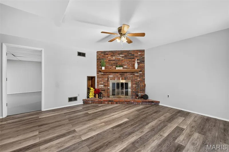 Spacious living area featuring wood-finish flooring, a brick-surround fireplace with hearth, and a wood mantel — 1319 Brandywine Lane, St Peters, MO 63376