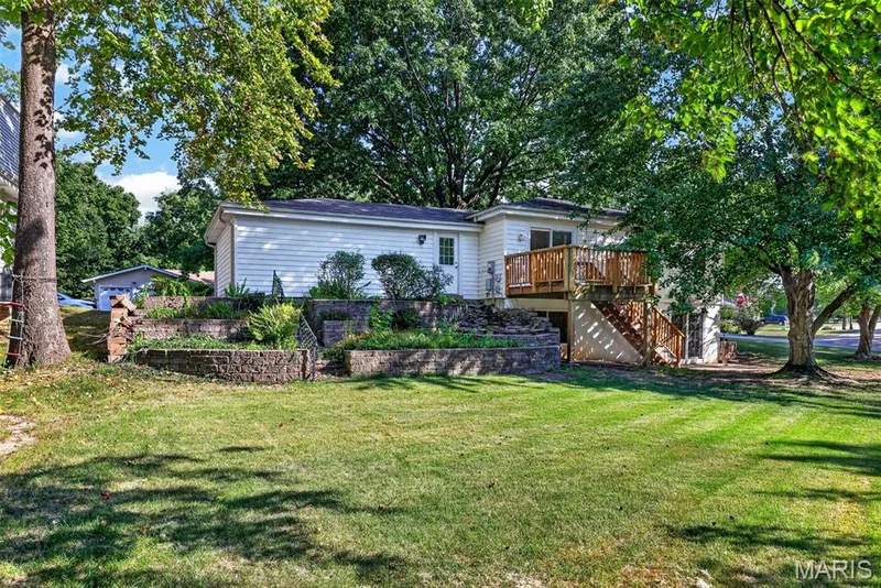 Expansive rear yard featuring a wood deck with stairs, built-in planters with retaining walls, and mature trees — 1319 Brandywine Lane, St Peters, MO 63376