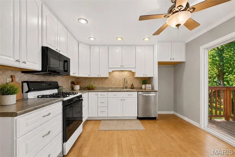 White cabinetry with chrome hardware, dark countertop, tile backsplash, and light wood-finish flooring — 1319 Brandywine Lane, St Peters, MO 63376