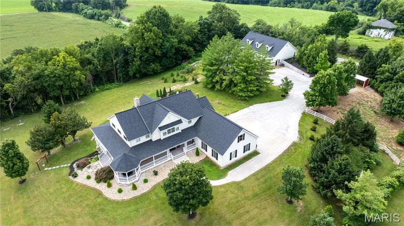 Expansive property featuring a residence with a large covered porch, an auxiliary building, mature trees, and a gravel driveway — 205 Howell Road, Defiance, MO 63341