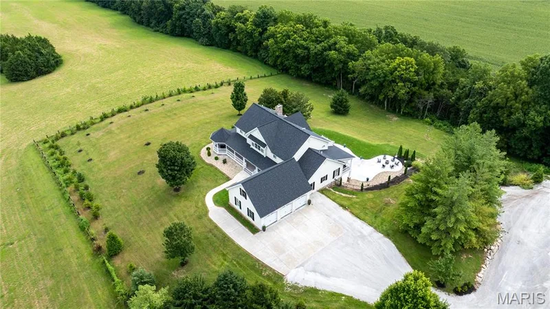Expansive property featuring a large residence, attached garage, concrete driveway, and outdoor patio area — 205 Howell Road, Defiance, MO 63341