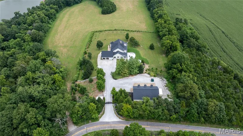 Aerial view showcasing a sophisticated residence set on expansive grounds with mature tree-lined perimeter, circular driveway approach, and a modern addition featuring solar panel installation — 205 Howell Road, Defiance, MO 63341